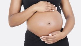 Mid section of pregnant woman touching abdomen over white background