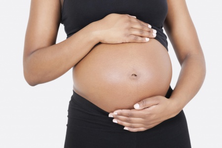 Mid section of pregnant woman touching abdomen over white background
