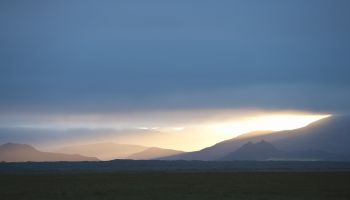 Sunlight coming through the clouds over a landscape of mountains and fields, Iceland.