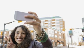 Woman photographing herself with smart phone on city street