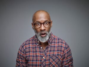 Portrait of astonished man wearing spectacles and checked shirt in front of grey background