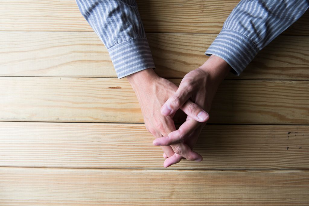 Close up on male hands folded in prayer at a wooden table
