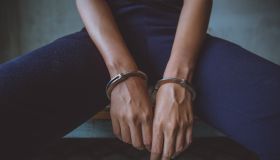Midsection Of Woman Wearing Handcuffs Sitting In Prison