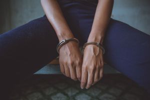Midsection Of Woman Wearing Handcuffs Sitting In Prison