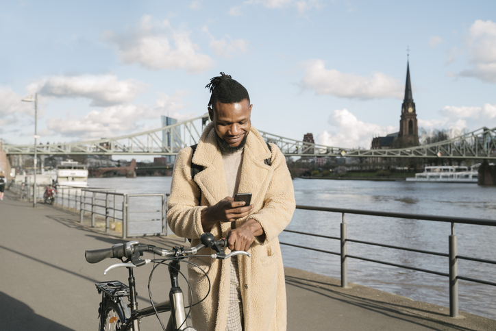 Stylish man with a bicycle using smartphone on riverbank, Frankfurt, Germany